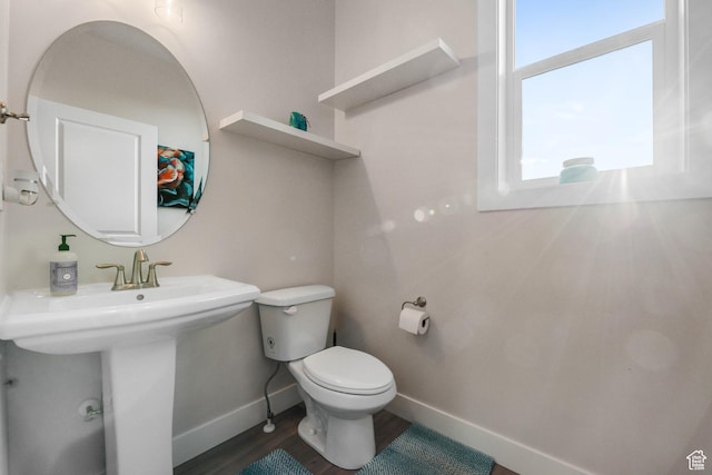 half bath with toilet, baseboards, wood finished floors, and a sink