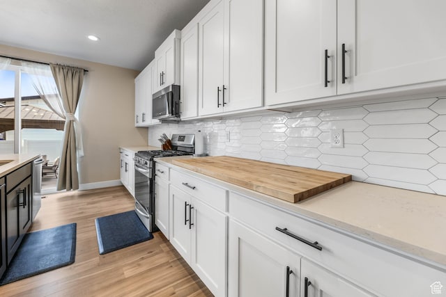 kitchen featuring tasteful backsplash, baseboards, light wood-style flooring, white cabinets, and stainless steel appliances