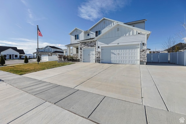 view of front of property with driveway, board and batten siding, stone siding, a garage, and fence