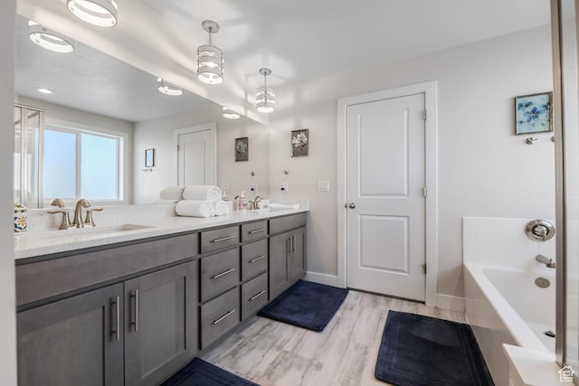 full bathroom with a garden tub, wood finished floors, a sink, double vanity, and baseboards