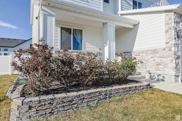 view of side of home with covered porch, fence, and stone siding