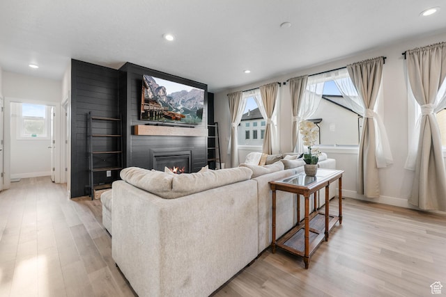 living area with light wood-style flooring, a large fireplace, baseboards, and recessed lighting