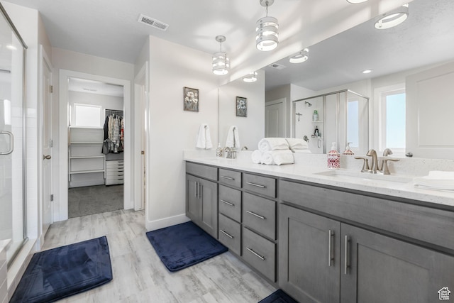 bathroom featuring visible vents, a sink, a walk in closet, a stall shower, and double vanity