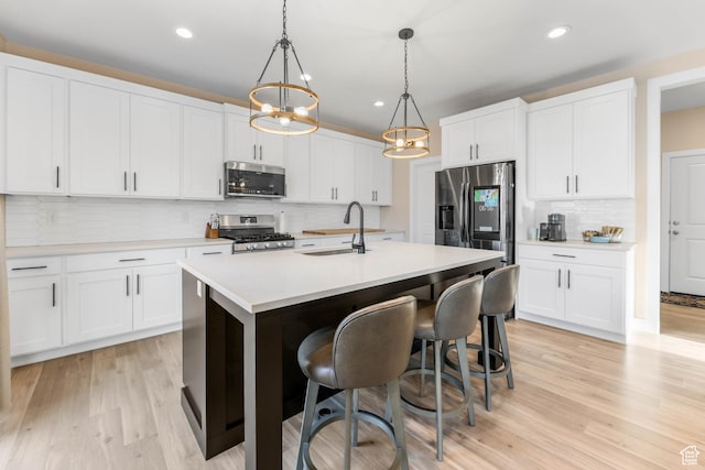 kitchen featuring tasteful backsplash, light countertops, a kitchen island with sink, stainless steel appliances, and a sink