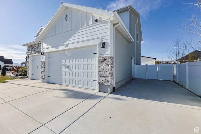 view of home's exterior featuring board and batten siding, stone siding, a garage, and concrete driveway