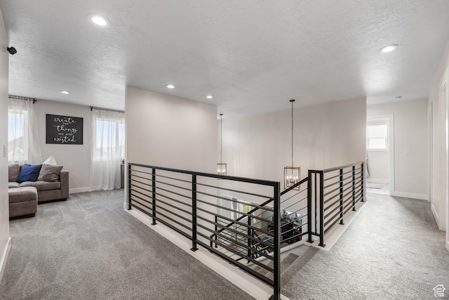 hall featuring a chandelier, a textured ceiling, carpet flooring, and an upstairs landing