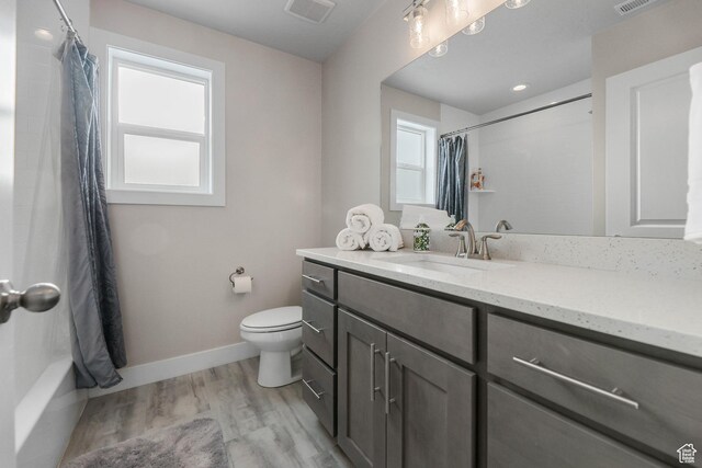 bathroom with toilet, a healthy amount of sunlight, wood finished floors, and visible vents