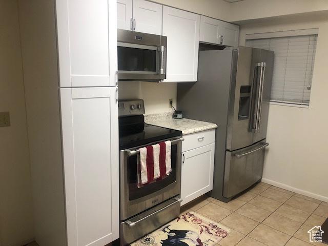 kitchen featuring stainless steel appliances, light tile patterned floors, light countertops, and white cabinetry