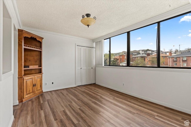 unfurnished bedroom featuring a textured ceiling, wood finished floors, a closet, and ornamental molding