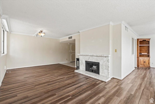 unfurnished living room featuring a high end fireplace, a textured ceiling, visible vents, wood finished floors, and baseboards