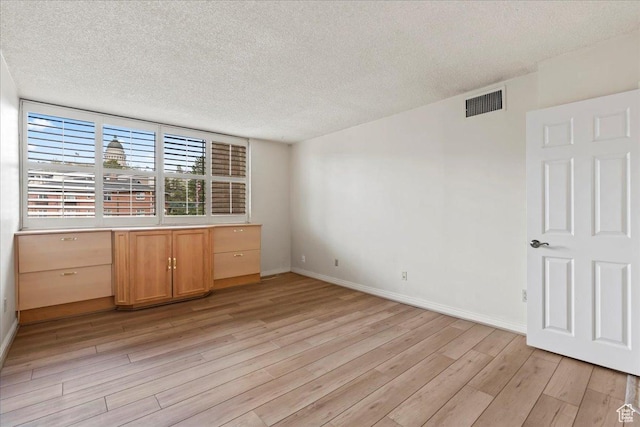 interior space featuring visible vents, baseboards, light wood finished floors, and a textured ceiling