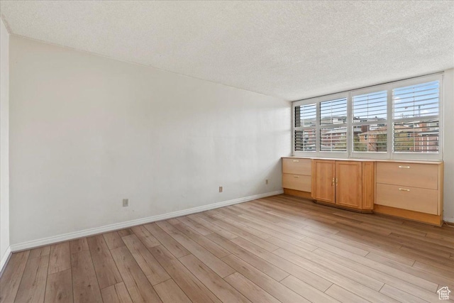 spare room featuring baseboards, light wood finished floors, and a textured ceiling