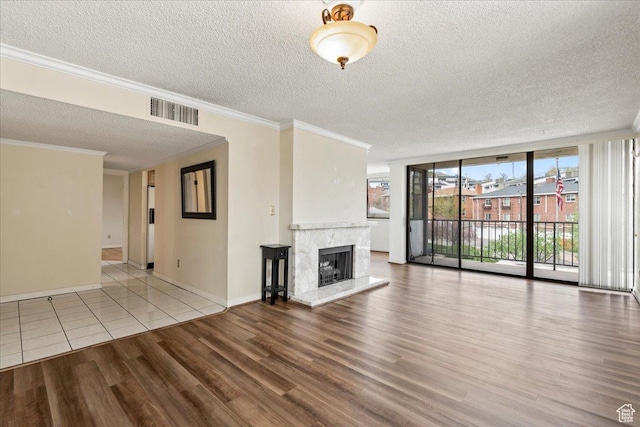 unfurnished living room with ornamental molding, a textured ceiling, visible vents, a high end fireplace, and wood finished floors