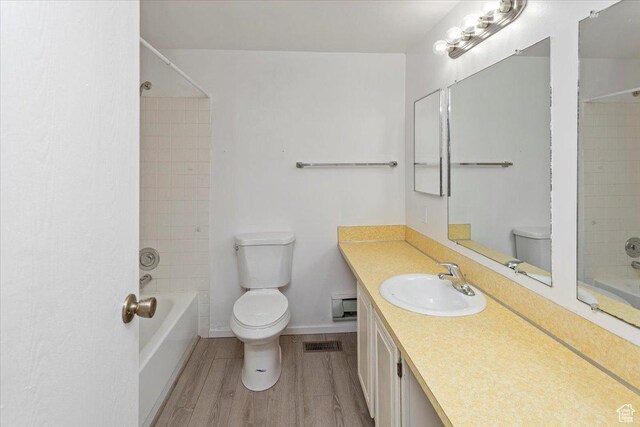 bathroom featuring visible vents, wood finished floors, toilet, and tub / shower combination