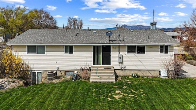 back of house featuring roof with shingles, a mountain view, and a lawn