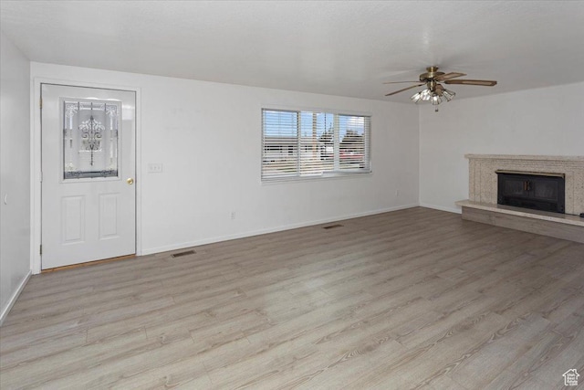 unfurnished living room with light wood-type flooring, a ceiling fan, visible vents, a high end fireplace, and baseboards
