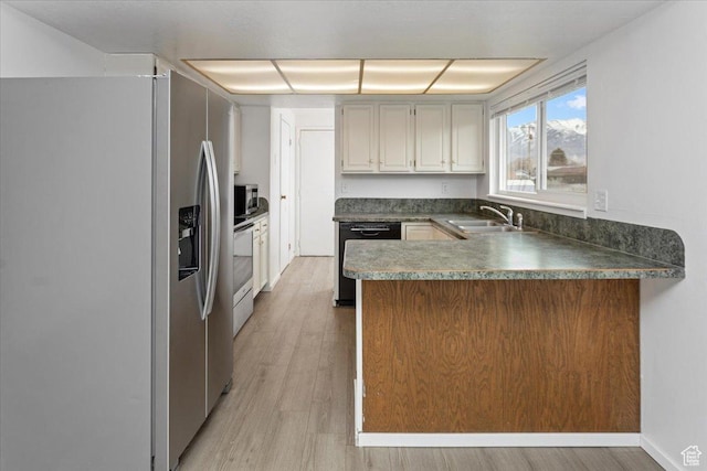 kitchen featuring a peninsula, light wood-type flooring, appliances with stainless steel finishes, dark countertops, and a sink