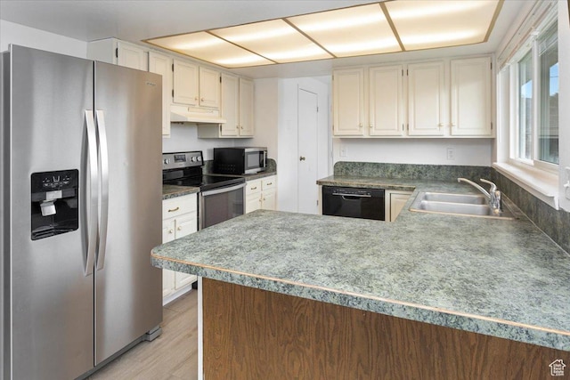 kitchen with a sink, appliances with stainless steel finishes, a peninsula, under cabinet range hood, and light wood-style flooring