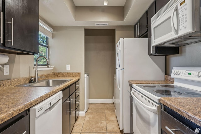 kitchen with white appliances, light tile patterned floors, visible vents, a raised ceiling, and a sink