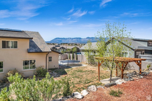view of yard with a trampoline, a mountain view, a pergola, and fence