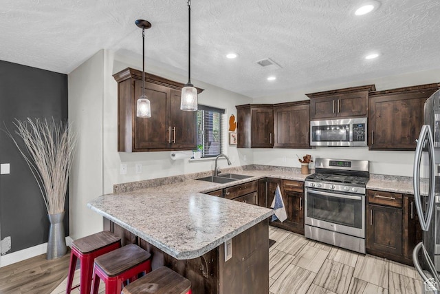 kitchen featuring dark brown cabinetry, a breakfast bar, a peninsula, stainless steel appliances, and a sink