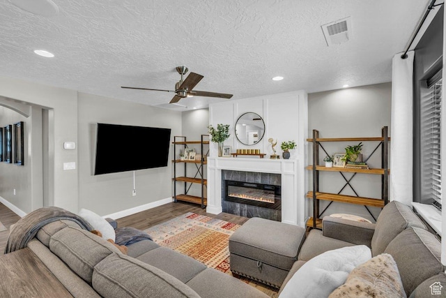 living room with a glass covered fireplace, baseboards, a textured ceiling, a ceiling fan, and wood finished floors