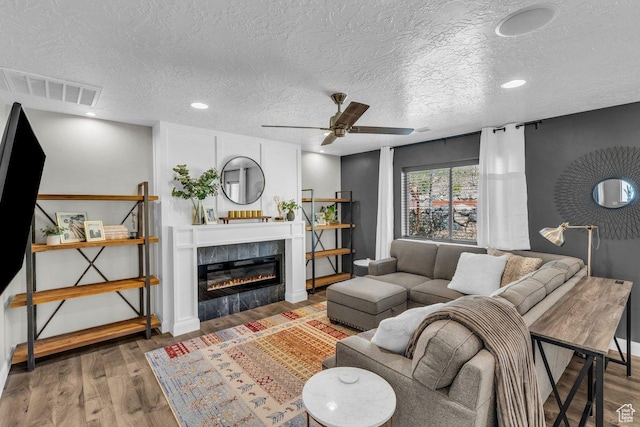 living room with a textured ceiling, a ceiling fan, visible vents, wood finished floors, and a tile fireplace