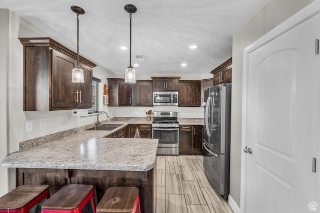 kitchen with a peninsula, light countertops, dark brown cabinets, appliances with stainless steel finishes, and a sink