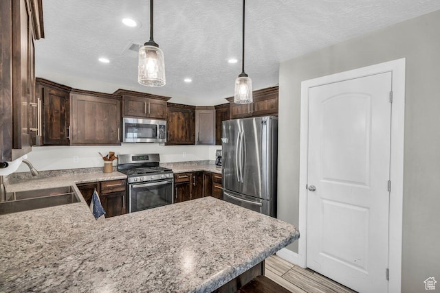 kitchen with dark brown cabinets, recessed lighting, appliances with stainless steel finishes, a sink, and hanging light fixtures