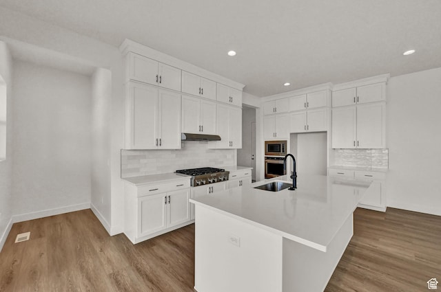 kitchen with appliances with stainless steel finishes, under cabinet range hood, a sink, backsplash, and baseboards