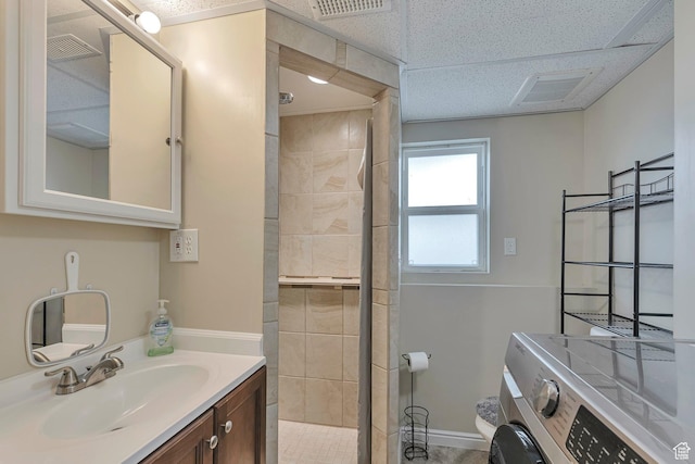 bathroom featuring tiled shower, vanity, visible vents, washer / dryer, and baseboards