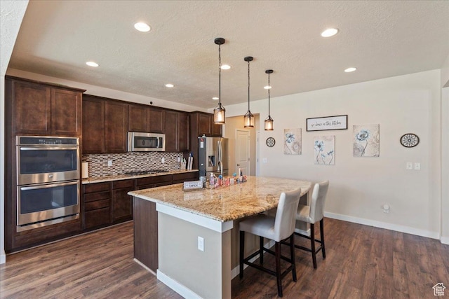 12133 S Broken Arch Ln, Herriman, UT 84096 - kitchen with stainless steel appliances, a kitchen island with sink, dark brown cabinetry, and dark wood-style floors