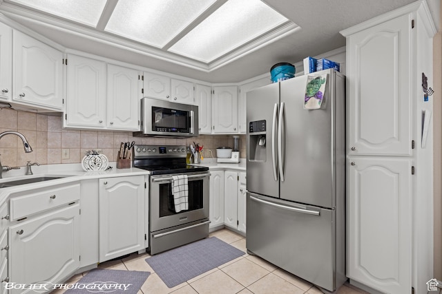 kitchen featuring white cabinets, appliances with stainless steel finishes, light tile patterned flooring, a sink, and backsplash