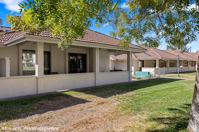 view of property exterior featuring stucco siding, a tiled roof, fence, and a lawn