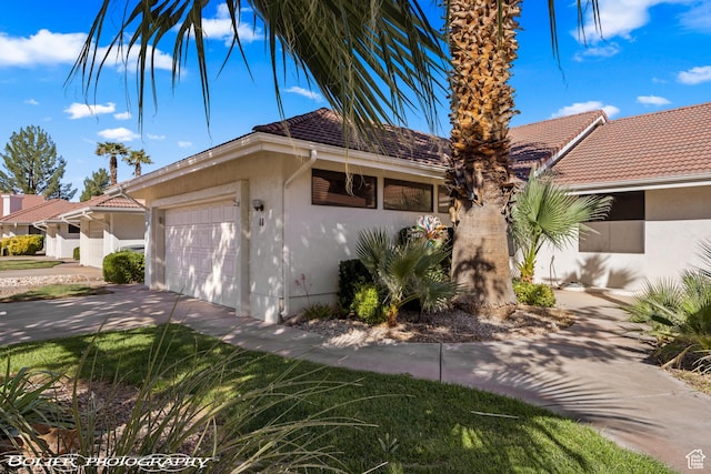 ranch-style home featuring a garage, driveway, stucco siding, and a tile roof