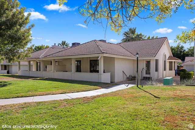 view of front of house featuring a tiled roof, a front lawn, a patio area, and stucco siding