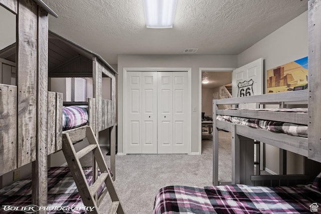 bedroom with carpet floors, a closet, visible vents, and a textured ceiling