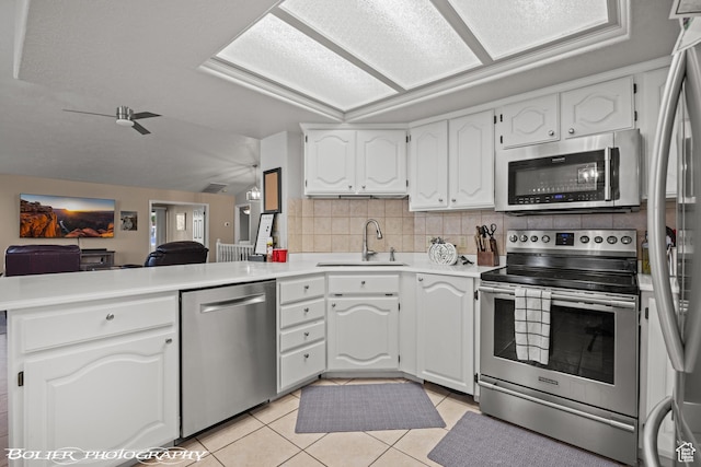 kitchen featuring a peninsula, backsplash, white cabinets, appliances with stainless steel finishes, and a sink