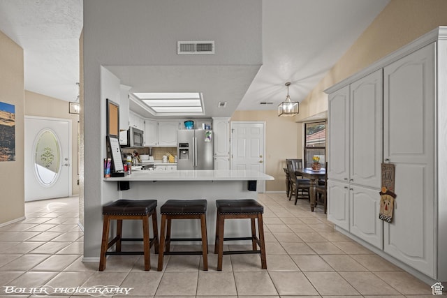kitchen featuring a peninsula, appliances with stainless steel finishes, light tile patterned floors, and visible vents