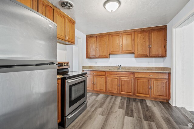 940 Fillmore Ave, Ogden, UT 84404 - kitchen with brown cabinets, wood finished floors, a sink, appliances with stainless steel finishes, and light stone counters