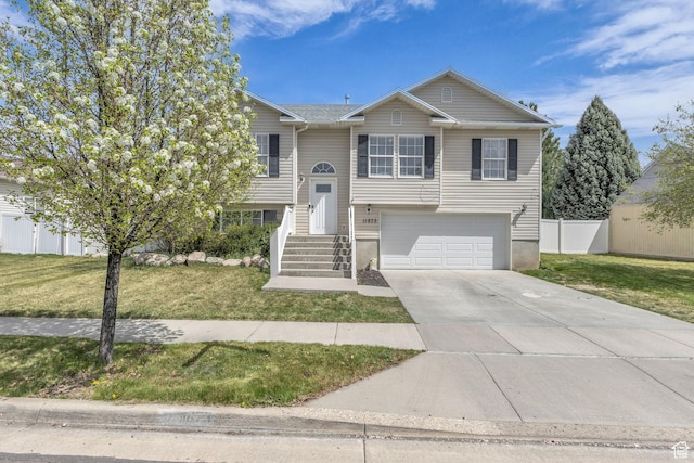 raised ranch with a garage, a front yard, fence, and concrete driveway