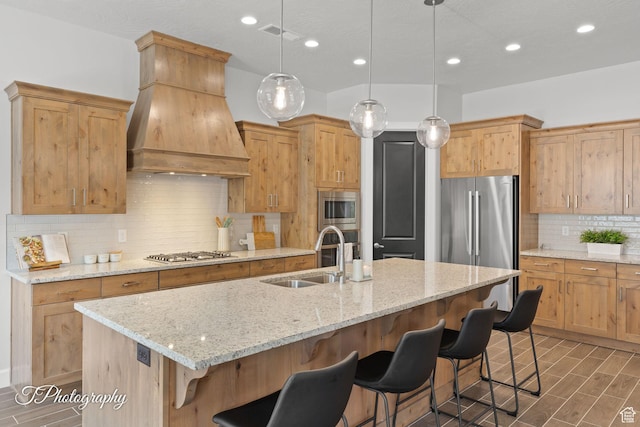 kitchen featuring an island with sink, a kitchen bar, a sink, stainless steel appliances, and custom range hood