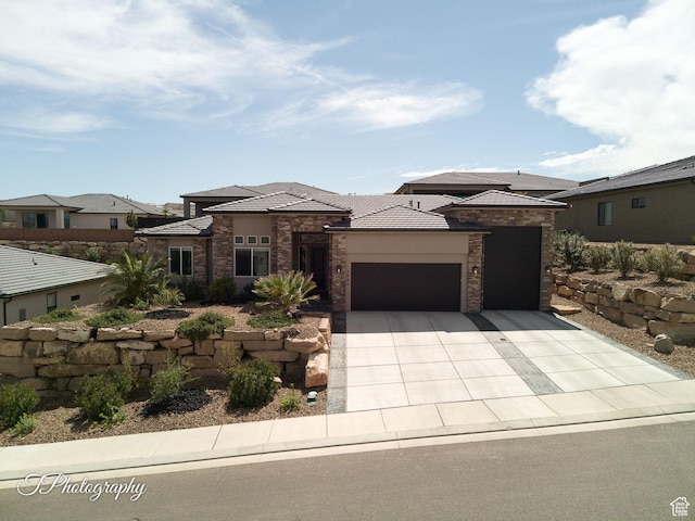 prairie-style home featuring a tiled roof, stucco siding, stone siding, an attached garage, and concrete driveway