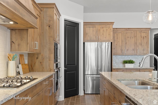 kitchen with light stone countertops, tasteful backsplash, a sink, stainless steel appliances, and premium range hood