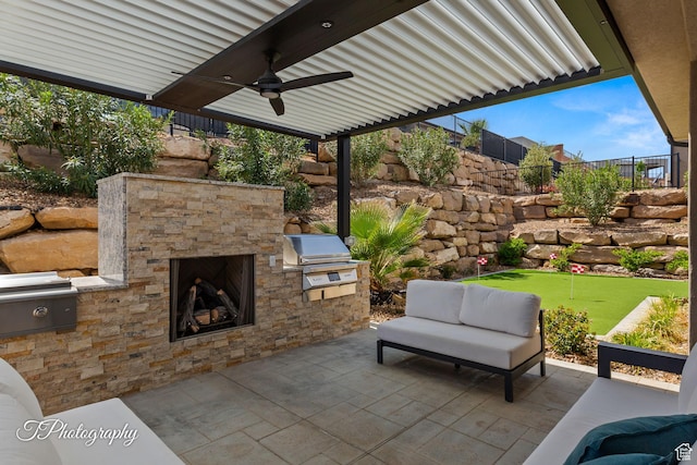 view of patio featuring area for grilling, an outdoor kitchen, a ceiling fan, fence, and an outdoor stone fireplace