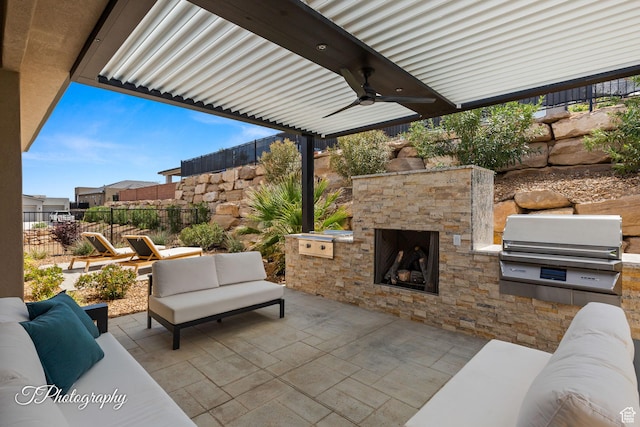 view of patio / terrace featuring ceiling fan, exterior kitchen, area for grilling, an outdoor living space with a fireplace, and fence