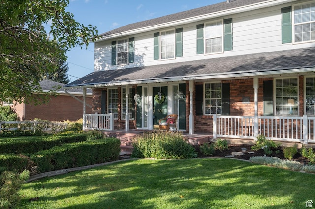 view of front of property featuring a front yard, a porch, brick siding, and roof with shingles