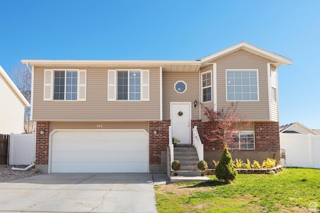 split foyer home featuring driveway, a front yard, brick siding, a garage, and fence