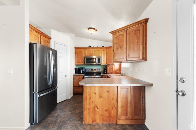 kitchen with appliances with stainless steel finishes, a peninsula, lofted ceiling, stone finish flooring, and a sink