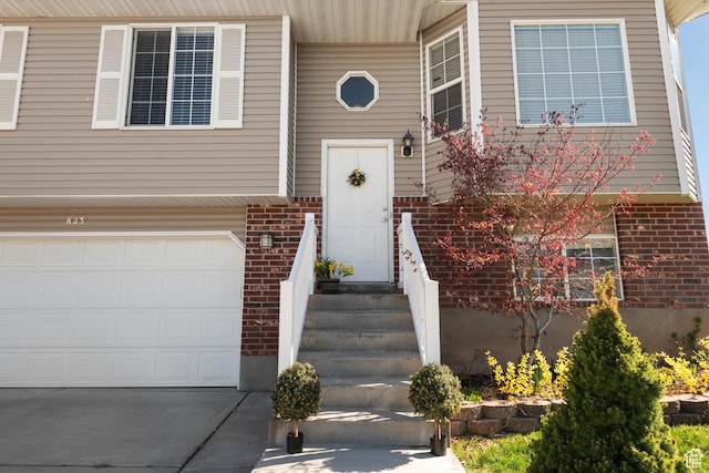 entrance to property with an attached garage, concrete driveway, and brick siding